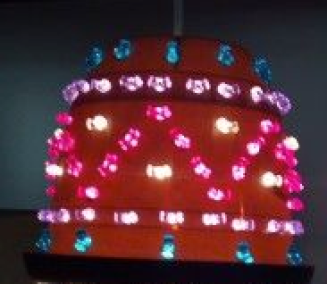 A planter with holes punched and colored beads inserted, over a light bulb.